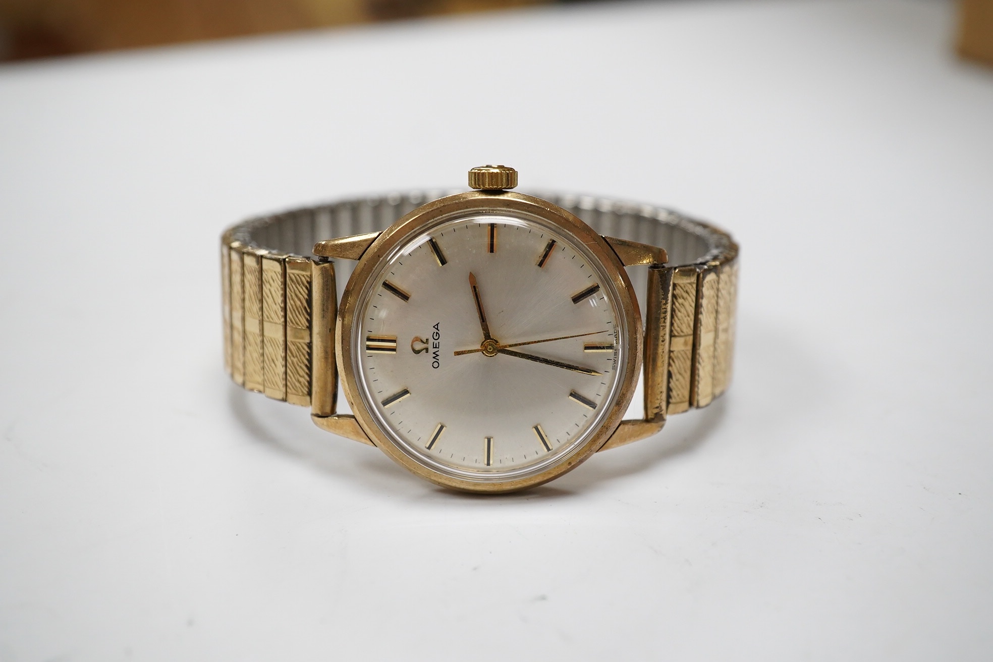 A gentleman's yellow metal Omega manual wind wrist watch, with baton numerals, case diameter 34mm, on an associated rolled gold flexible strap. Condition - fair